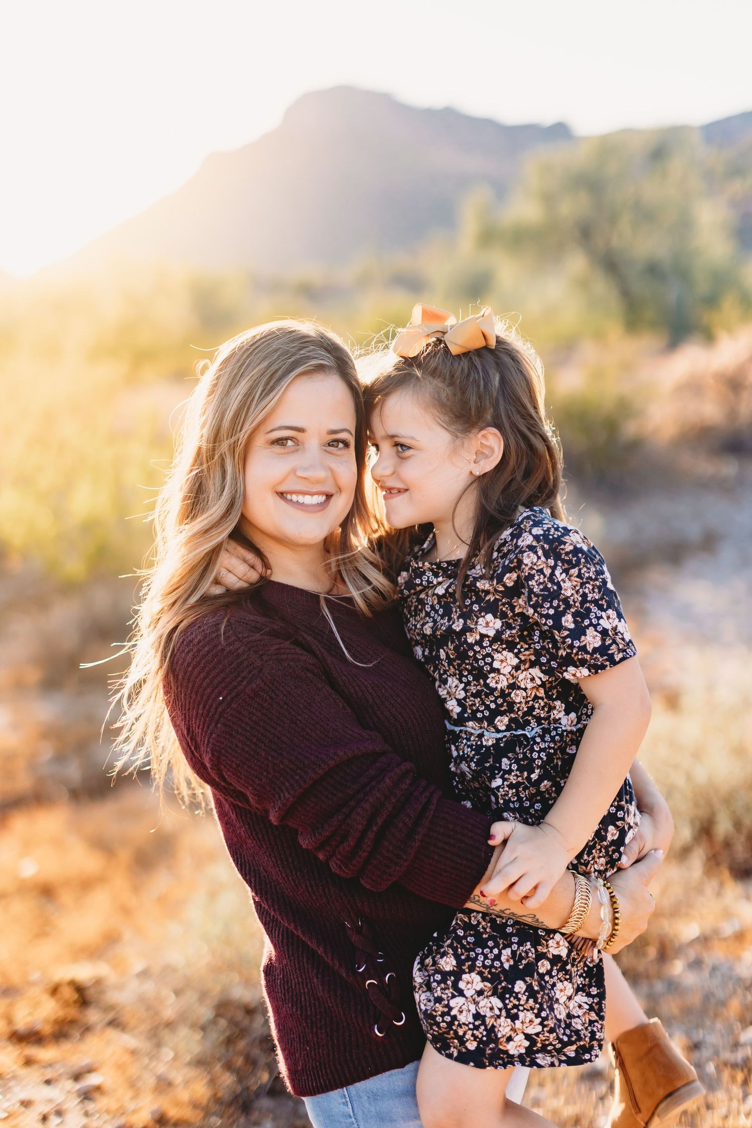 Candid moment between two people in burgundy sweater and floral dress against desert backdrop.
