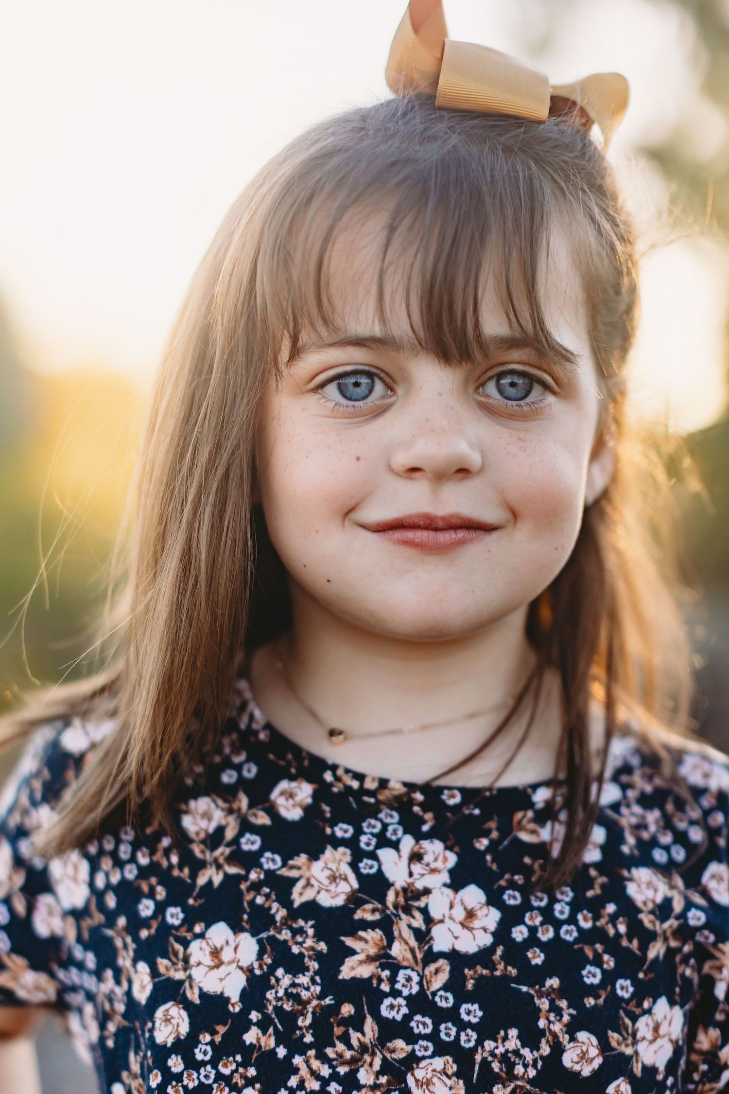 Close up portrait showing bright blue eyes and floral dress in golden sunset light.