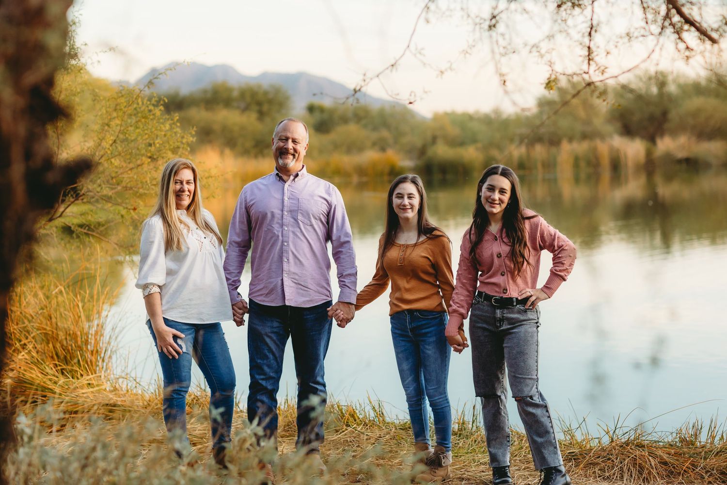 Group photo by lake with autumn trees and natural landscape in background.