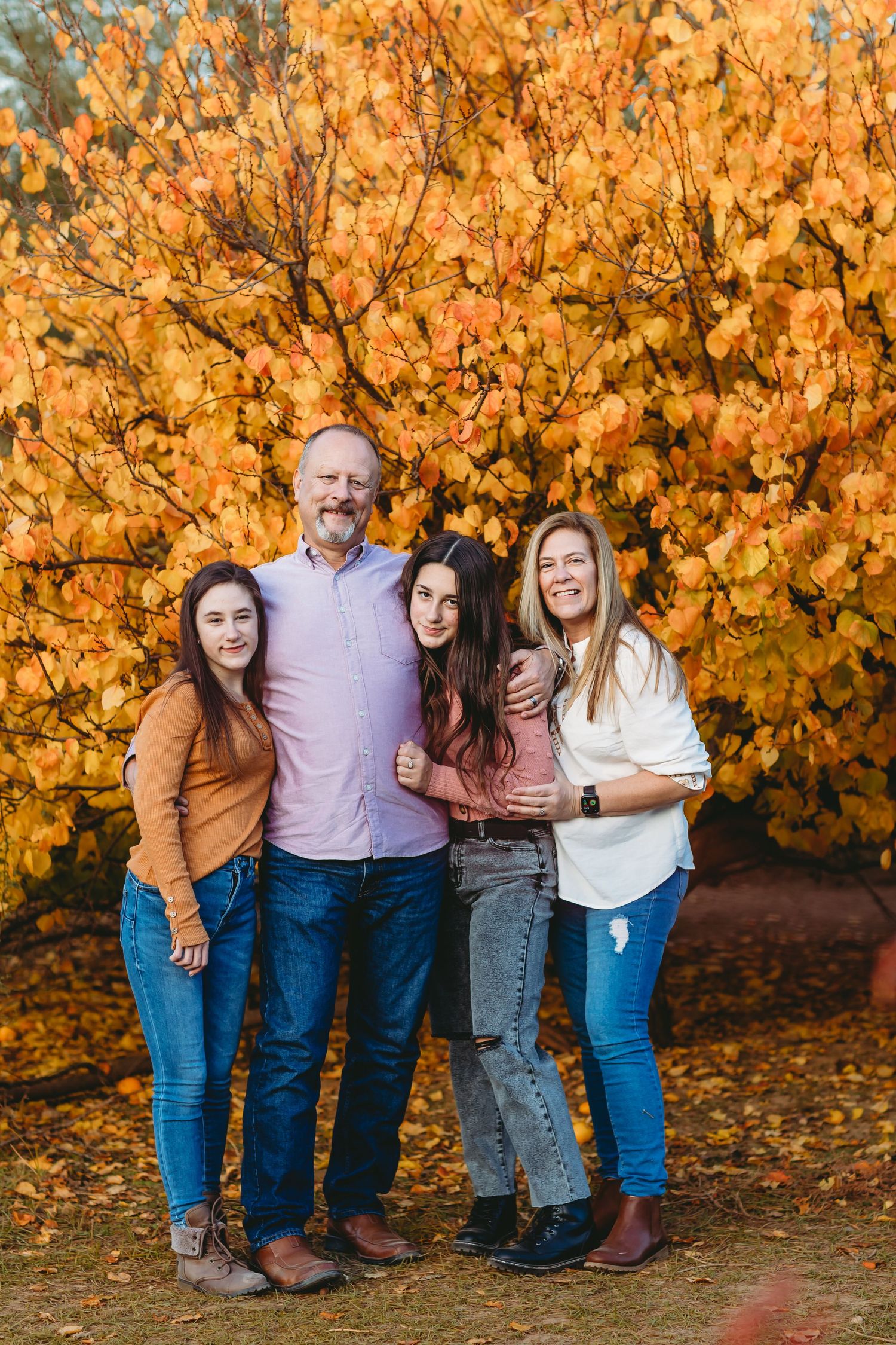 Family group poses together against backdrop of golden fall foliage.