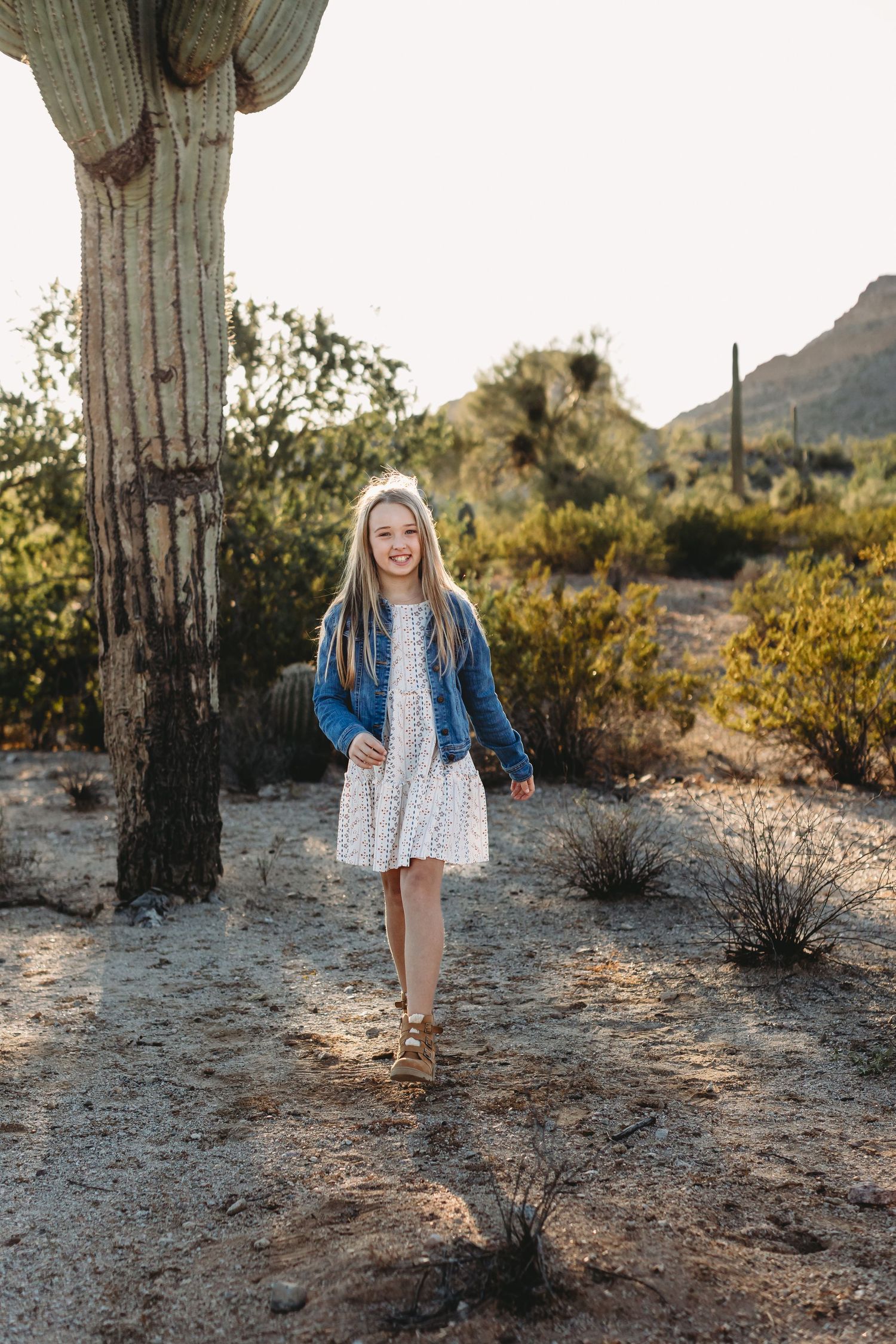 A young child explores around a giant saguaro cactus in the desert landscape.