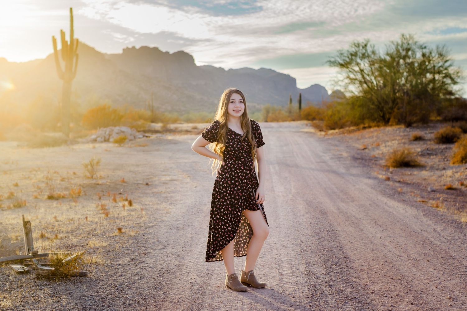 Woman in polka dot dress poses on desert path at sunset with mountains and cacti.