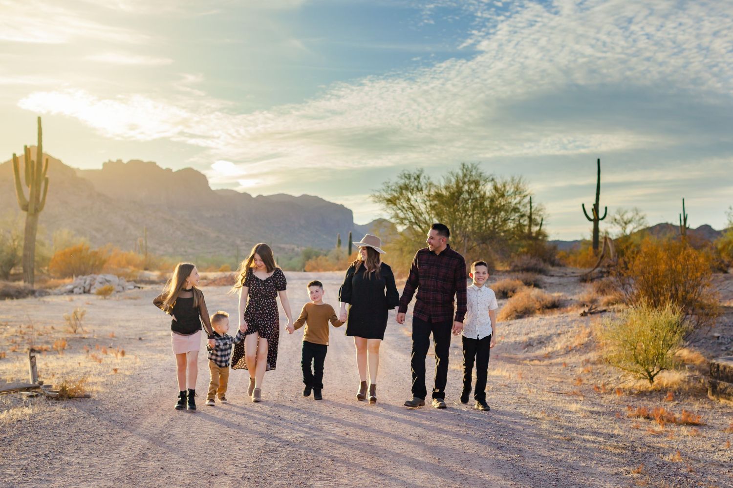 Family walking together on desert trail with mountain backdrop at sunset.