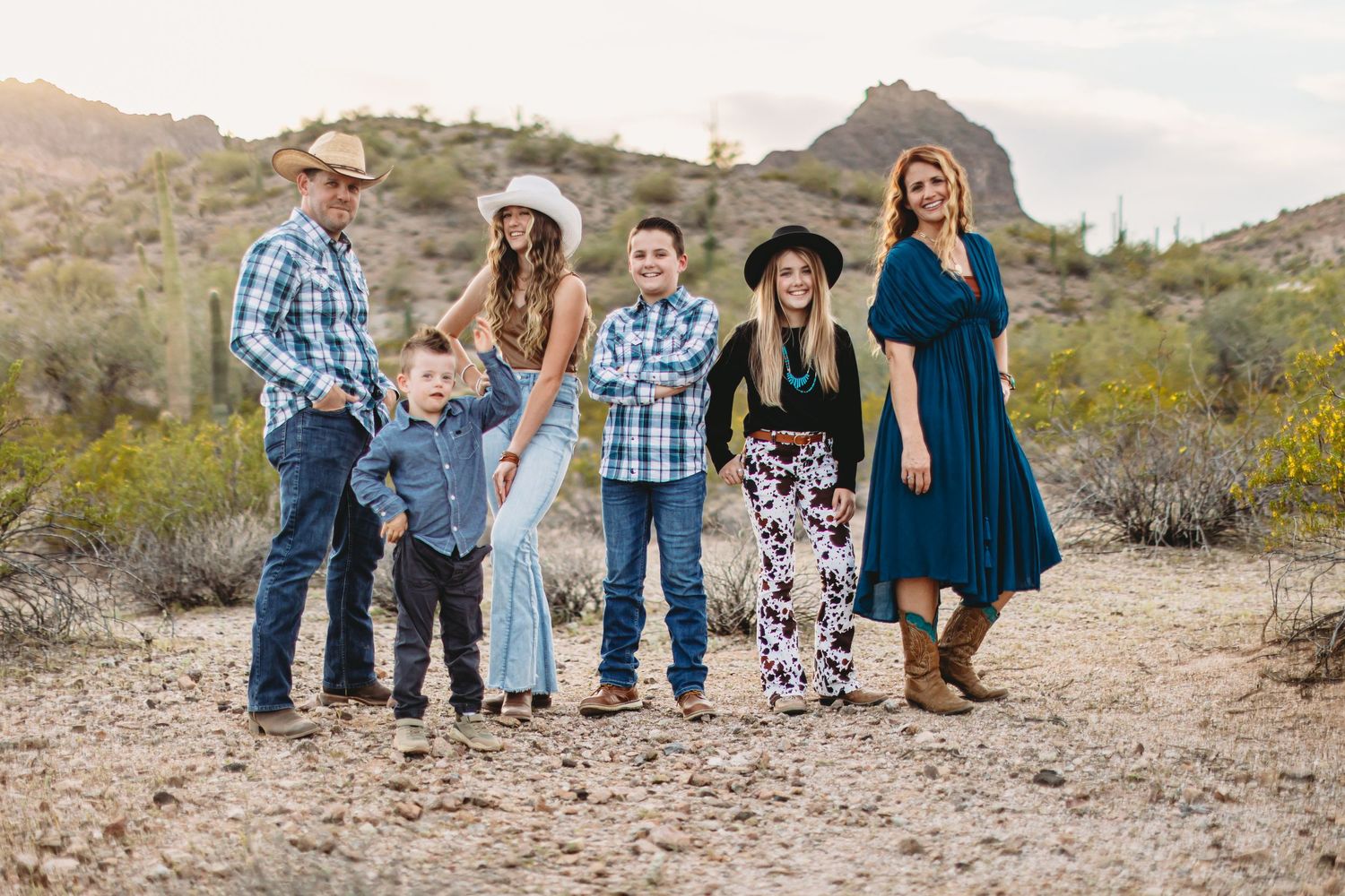 Family group poses on desert trail with mountain peaks and saguaro cacti in the background.