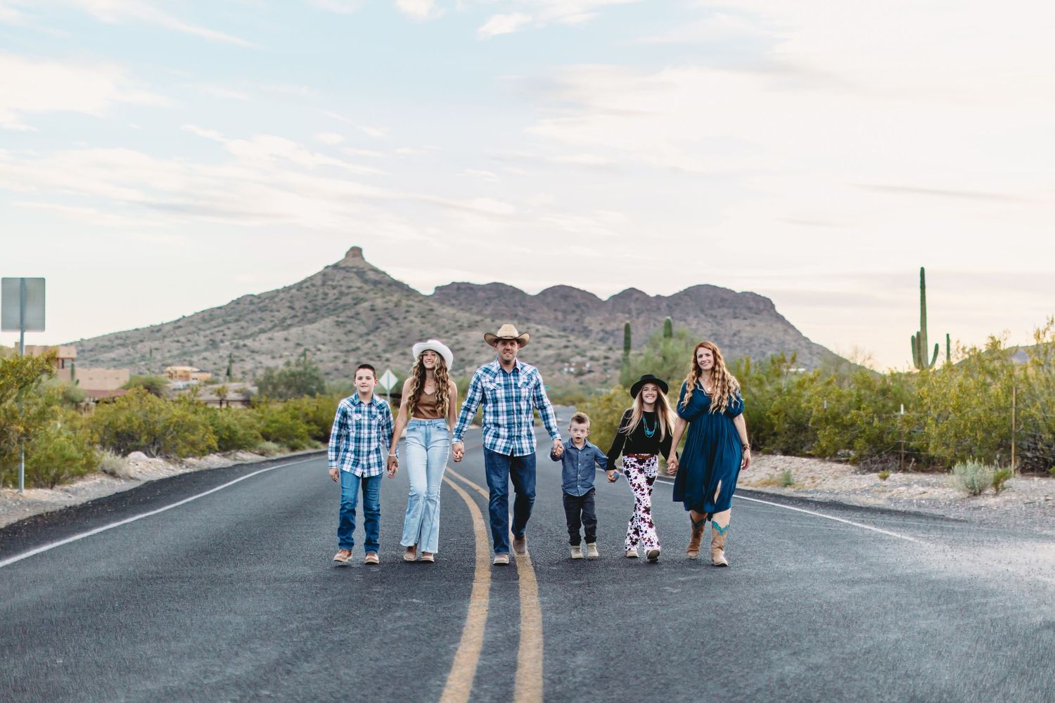 Group walking together down middle of desert road with mountain backdrop.