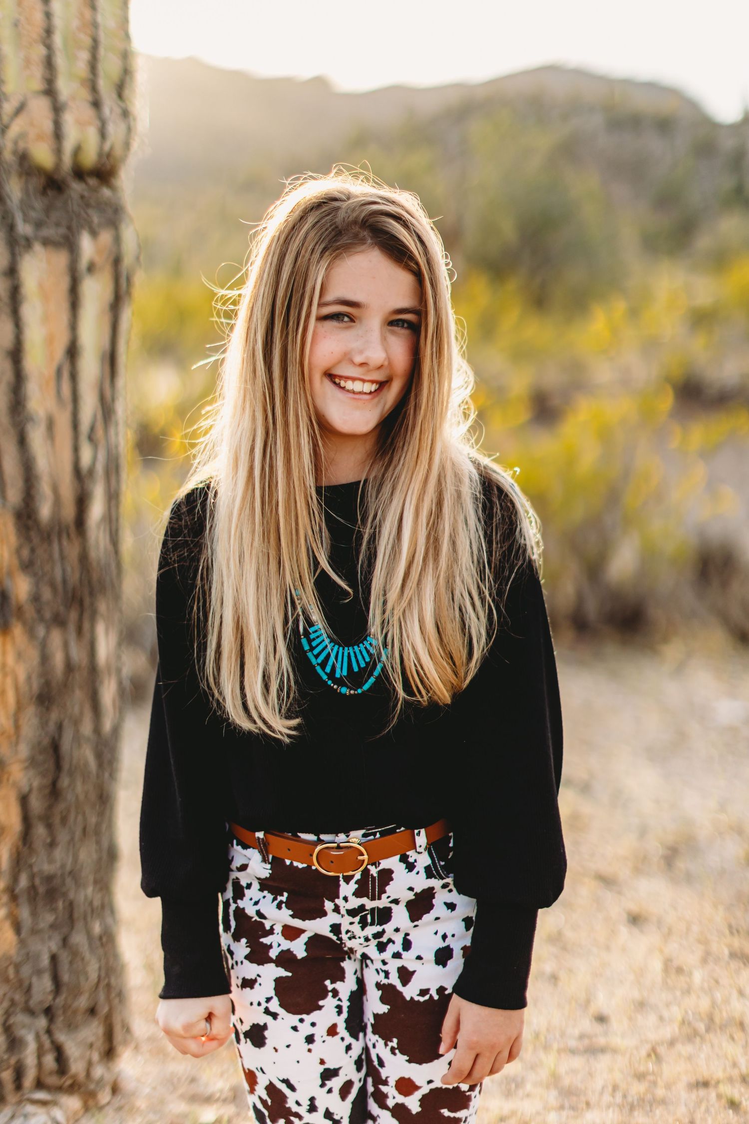 Portrait of person wearing black sweater and turquoise necklace against desert background.