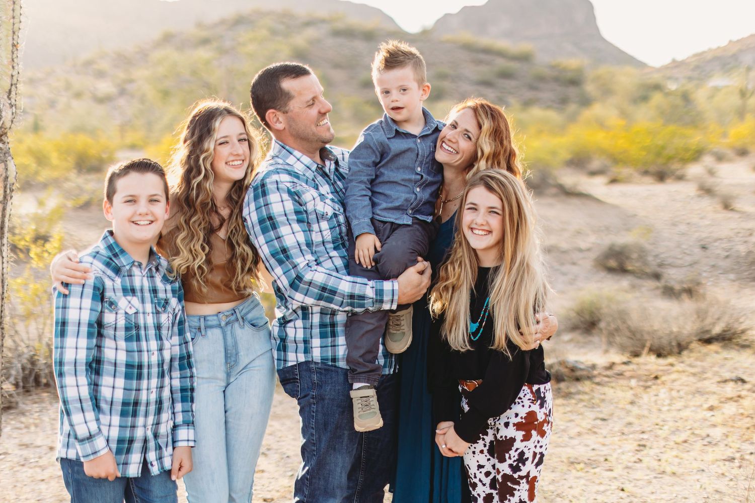 A family group poses together in the Arizona desert with mountains and cacti in the background.