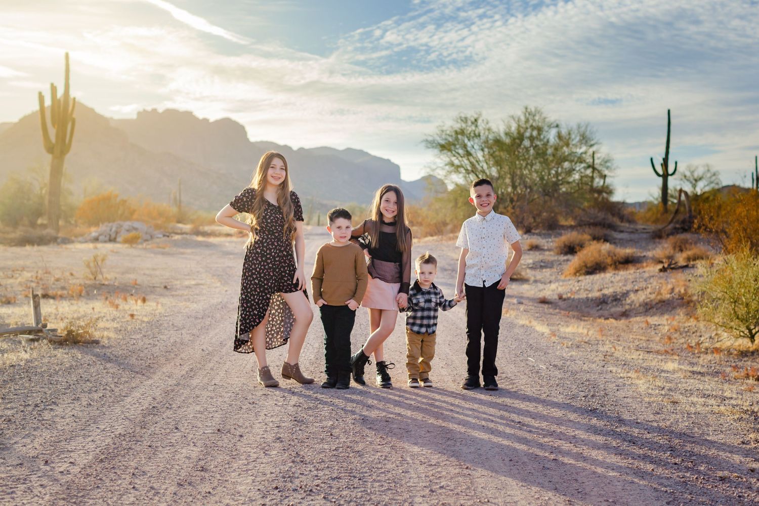 Family walking together on a desert path with saguaro cacti and mountains in the background.