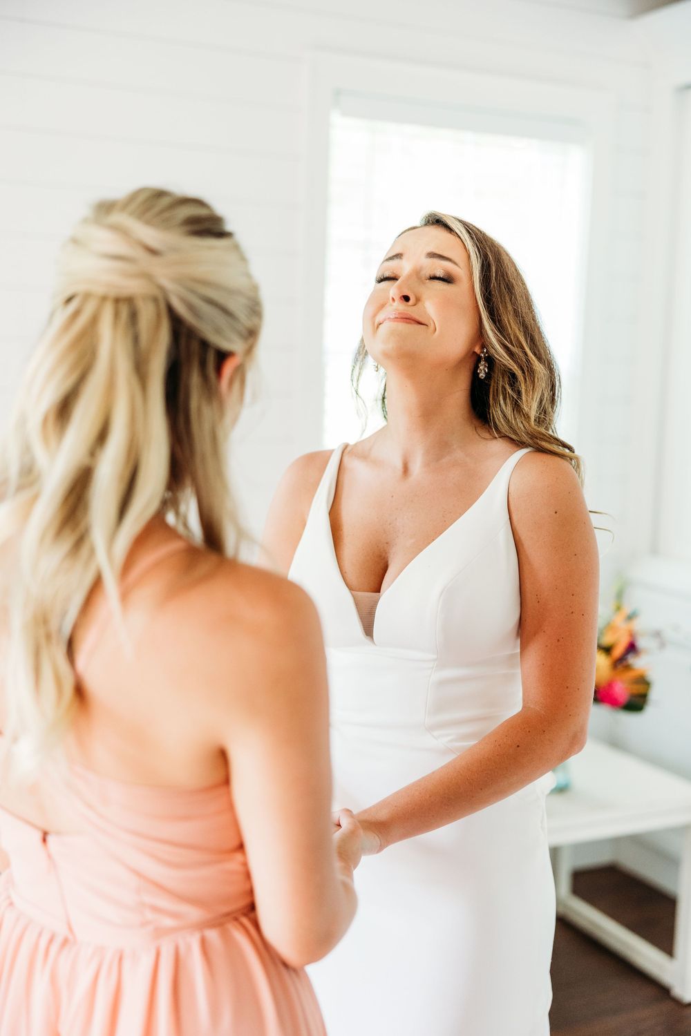 Bride in white dress getting ready with bridesmaid in peach dress.