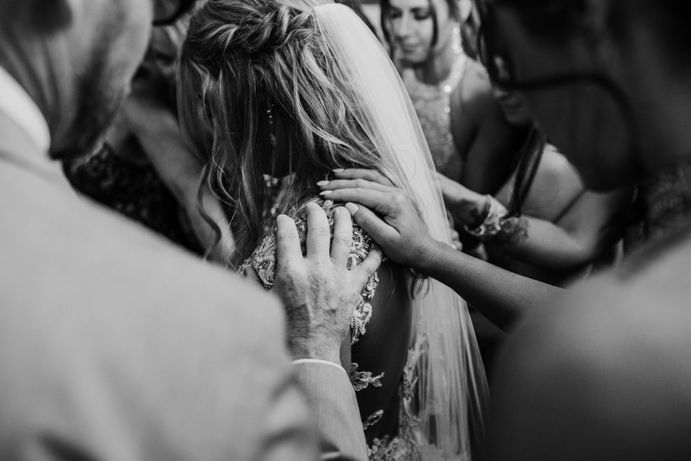An emotional wedding ceremony moment showing hands placing a veil with guests in background.
