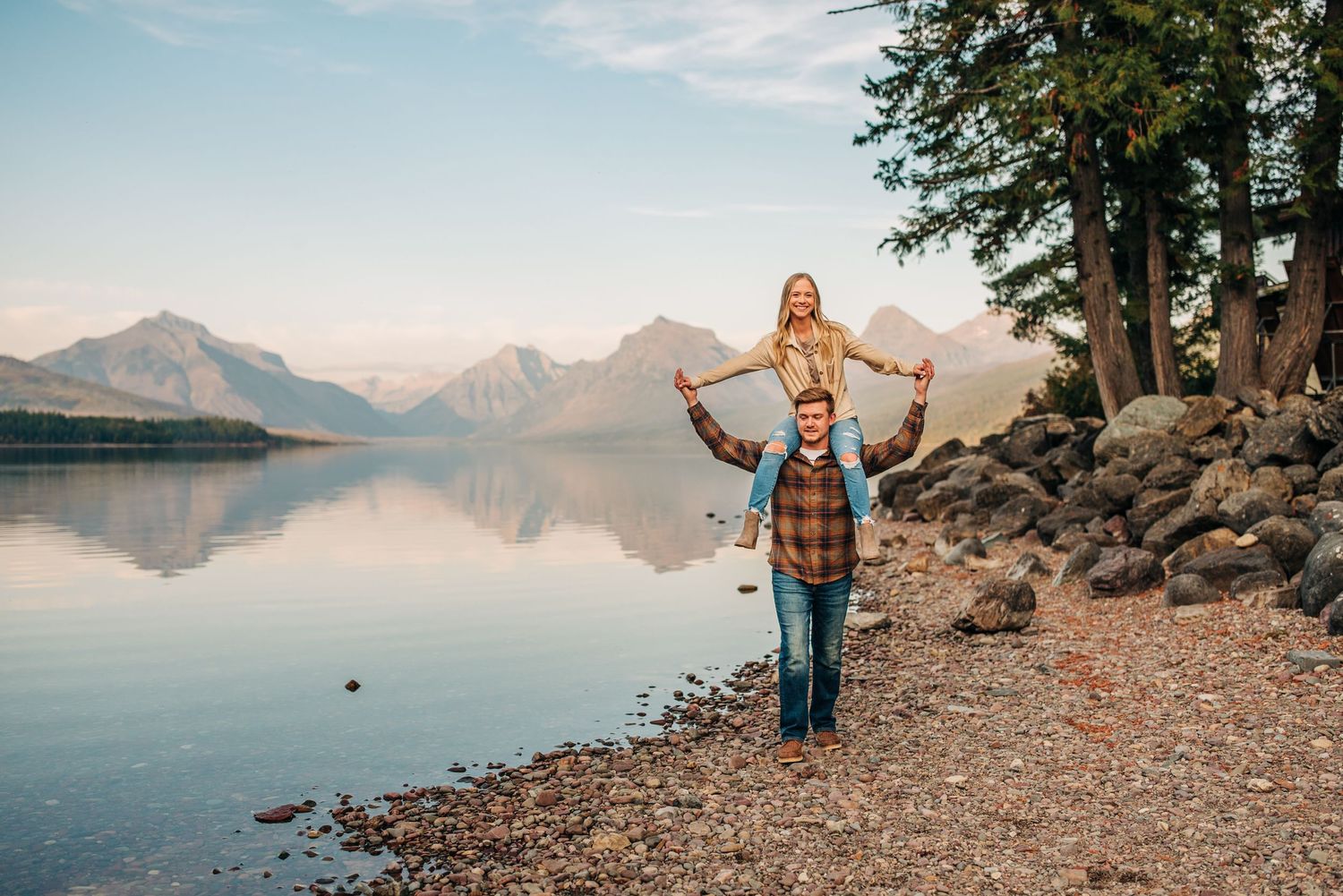 Couple walking along lake McDonald, girl sitting on guys shoulders. Couples engagement session.