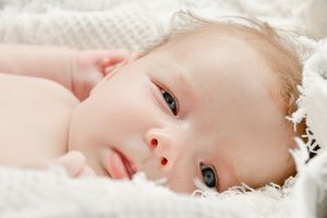 Close-up portraits of baby lying on white textured blanket showing peaceful expressions.