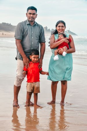 Family standing together at beach with waves and coastline in background.