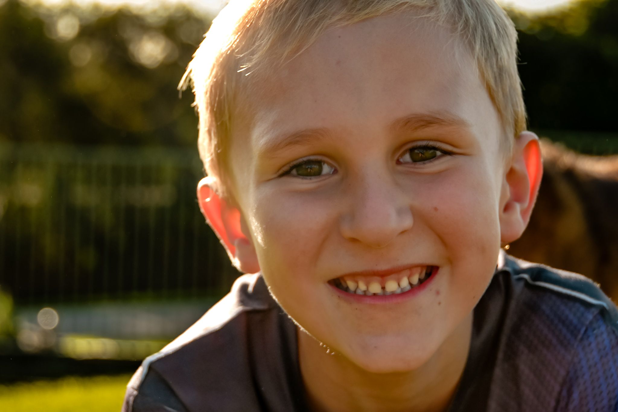 Young child smiles warmly at camera during golden hour outdoor portrait session.