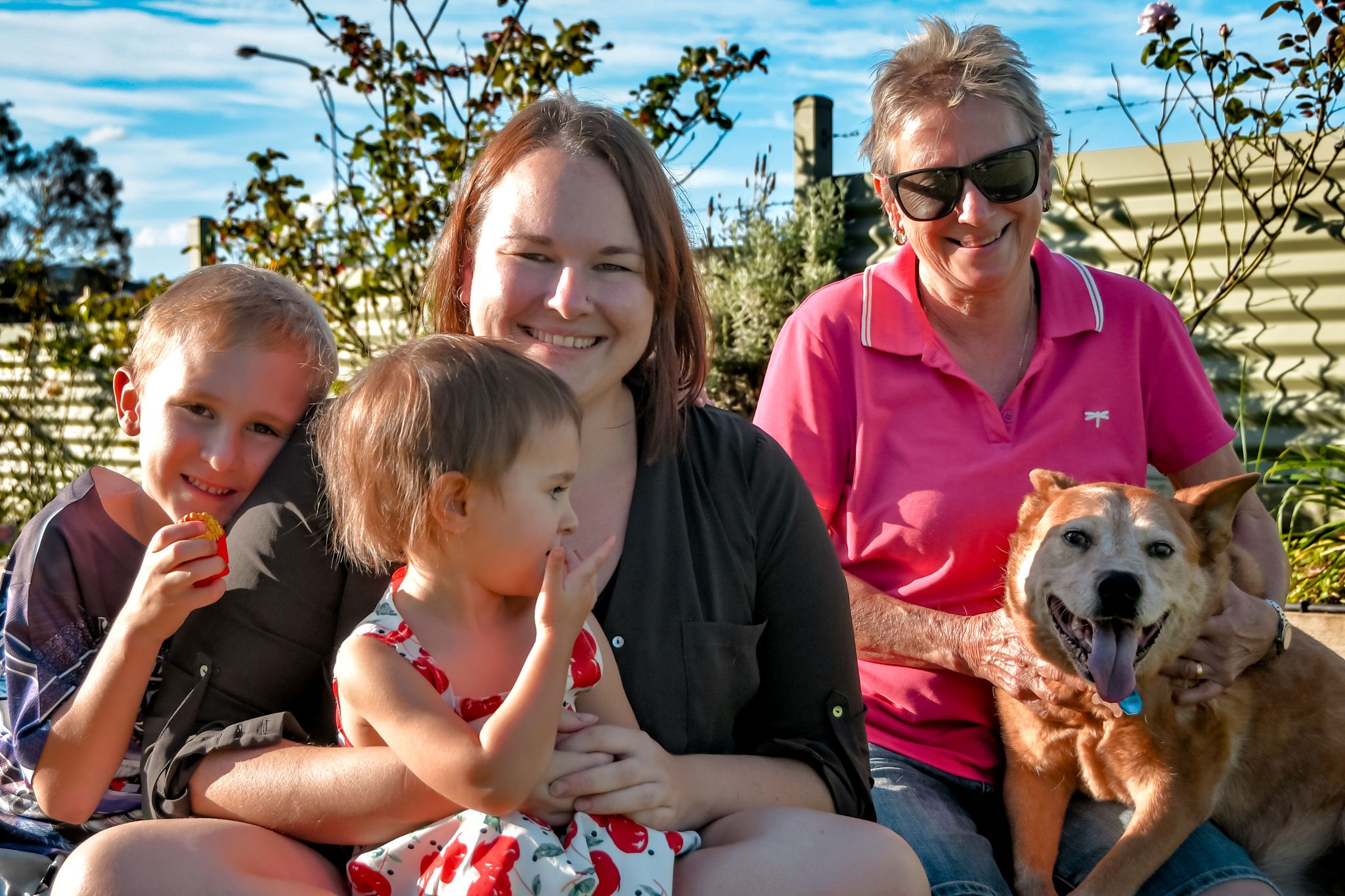 Family group sits outdoors with their dog on a sunny day.