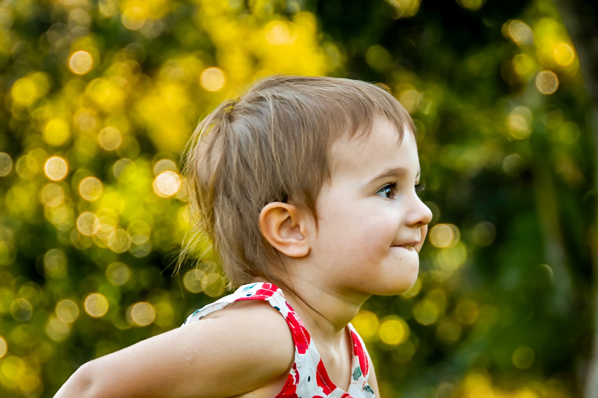 Child in red and white outfit looks to side with golden bokeh background.