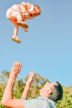 Parent tossing joyful baby in the air against bright blue sky on sunny day.