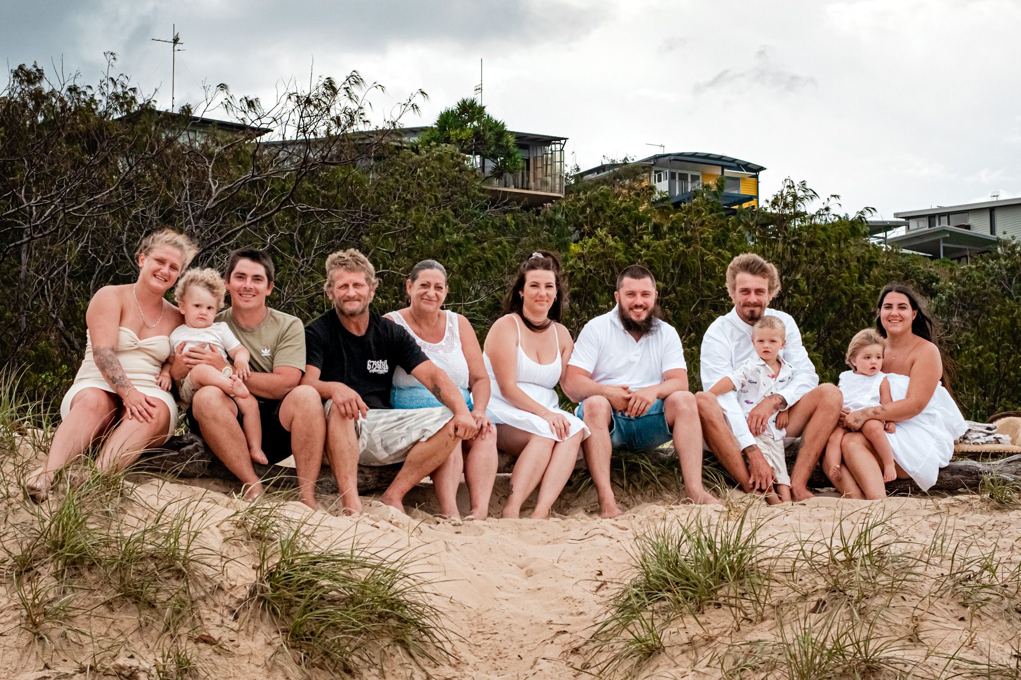 Group relaxing together on sandy beach dune under cloudy sky.