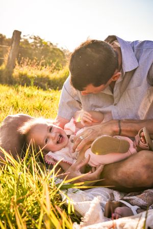 Family lying in sunlit grass sharing playful moments together at sunset.