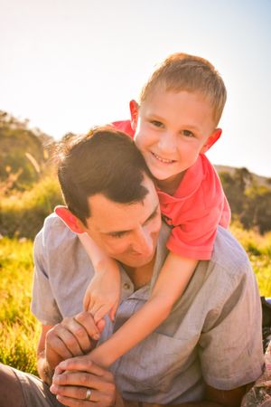 Father and child playing together in golden sunlit field during outdoor photo session.