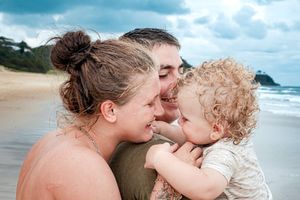 Intimate family moment captured at a scenic beach setting with waves and blue skies.