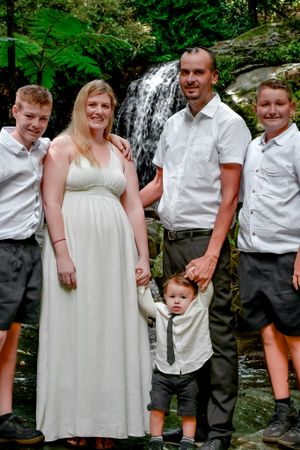 Family portrait session outdoors with everyone wearing coordinating white and black outfits near a waterfall.