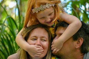 Playful family moment captured in lush green garden setting.