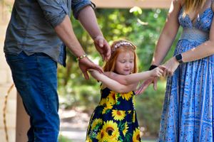 Family holding hands while walking through a sunlit garden with sunflowers.