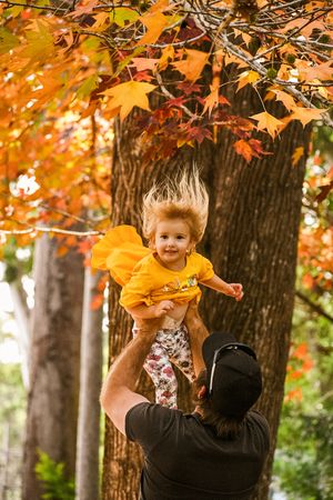 Child being lifted high among vibrant orange autumn leaves in the forest.