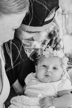 Black and white portrait of tender family moment with baby wearing lace headband.