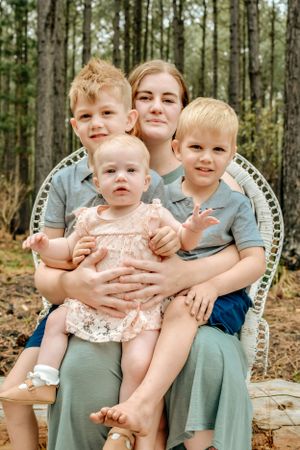 Family sitting together on a blanket in a pine forest wearing coordinated sage green outfits.