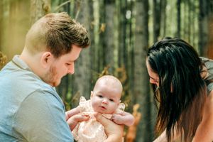 Natural light family photography session in a wooded setting with soft green background.