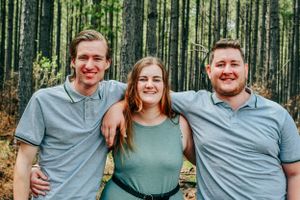 A family wearing coordinated grey and green outfits poses together in a forest setting.