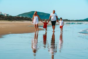 Family members walking along shoreline leaving footprints in wet sand at beach.