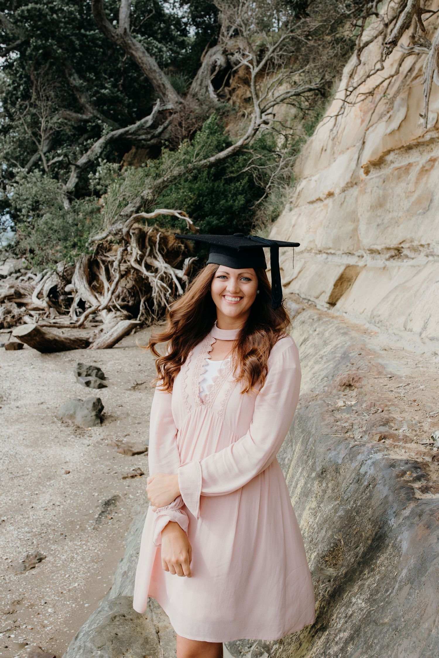 graduation photoshoot at the beach woman wears pink dress and graduation cap