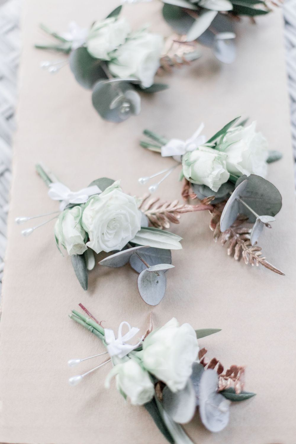 Delicate white and sage green floral boutonnieres lined up on light gray surface.