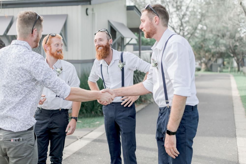 grooms party in pants and suspenders greeting wedding guest before ceremony while laughing and smiling
