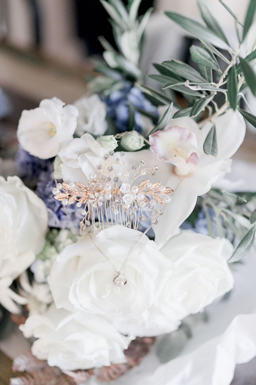 blue and white bridal bouquet detail with rose gold and crystal hair comb, silver necklace  and pale green leaves