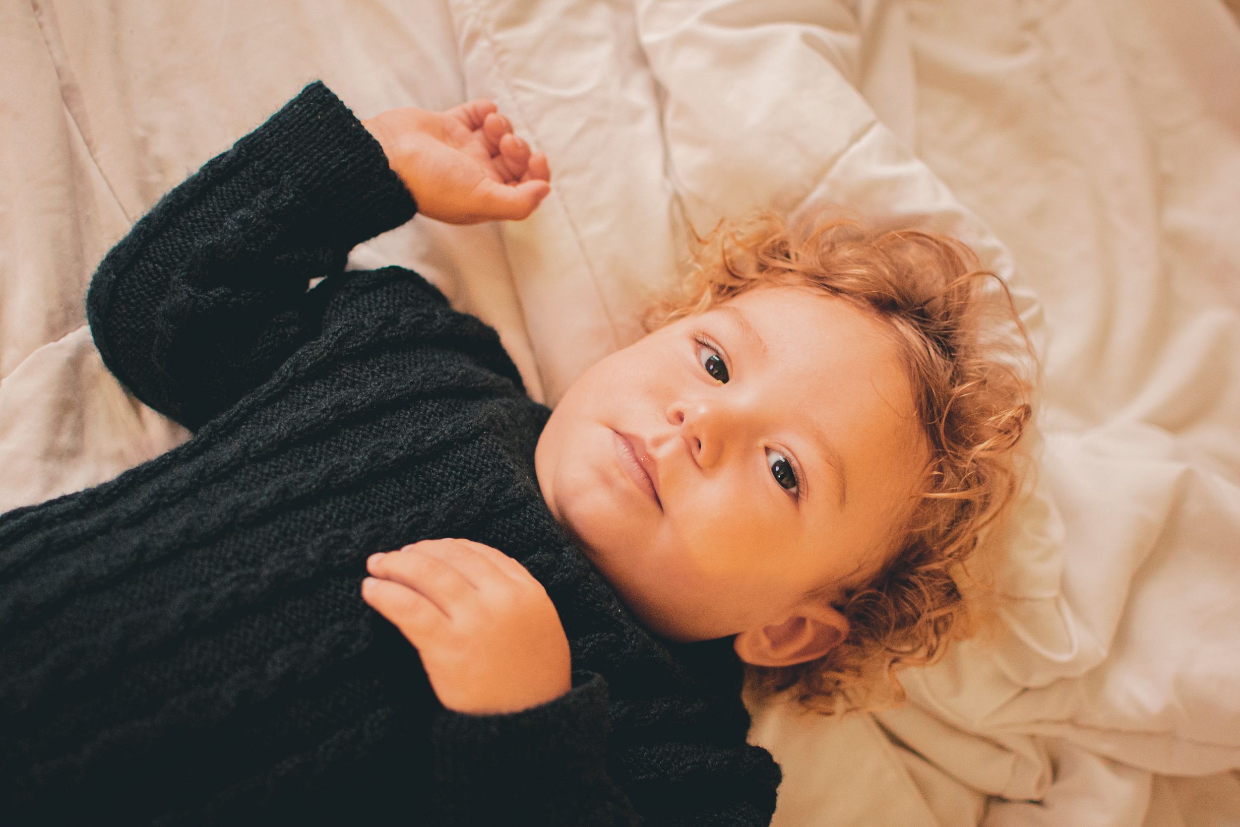 Young child with curly hair resting on beige sheets.
