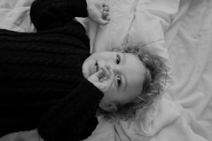 Black and white portrait of a child lying on light colored bedding.