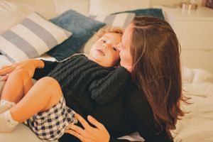 Mother and child share a joyful moment lying together on a bed with white linens and striped pillows.