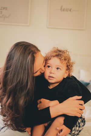 Intimate moment between parent and child wearing matching black tops on a comfortable bed.
