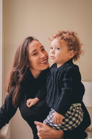 A sweet moment captured between parent and child both wearing black sweaters against a neutral wall.