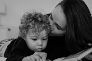 Black and white photo of parent and child reading together on white bedding.