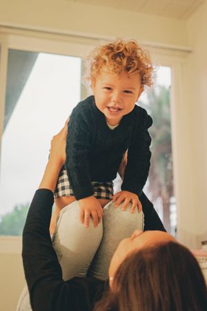 Playful indoor scene with curly-haired toddler in black sweater climbing and smiling.