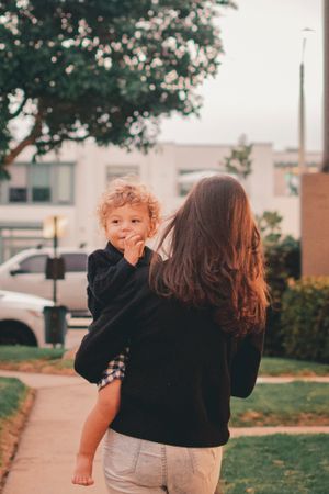 Outdoor family scene with curly-haired toddler in black sweater playing in warm sunset light.