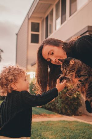 A heartwarming moment as a child pets a striped cat held by someone in a black sweater outdoors.
