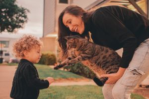 A joyful interaction between a tabby cat, child in black sweater, and person in casual wear outside.