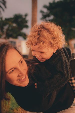 Parent and curly-haired toddler laughing together in warm sunset lighting.