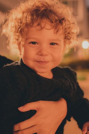 Close-up portrait of a smiling toddler with curly blonde hair at sunset.